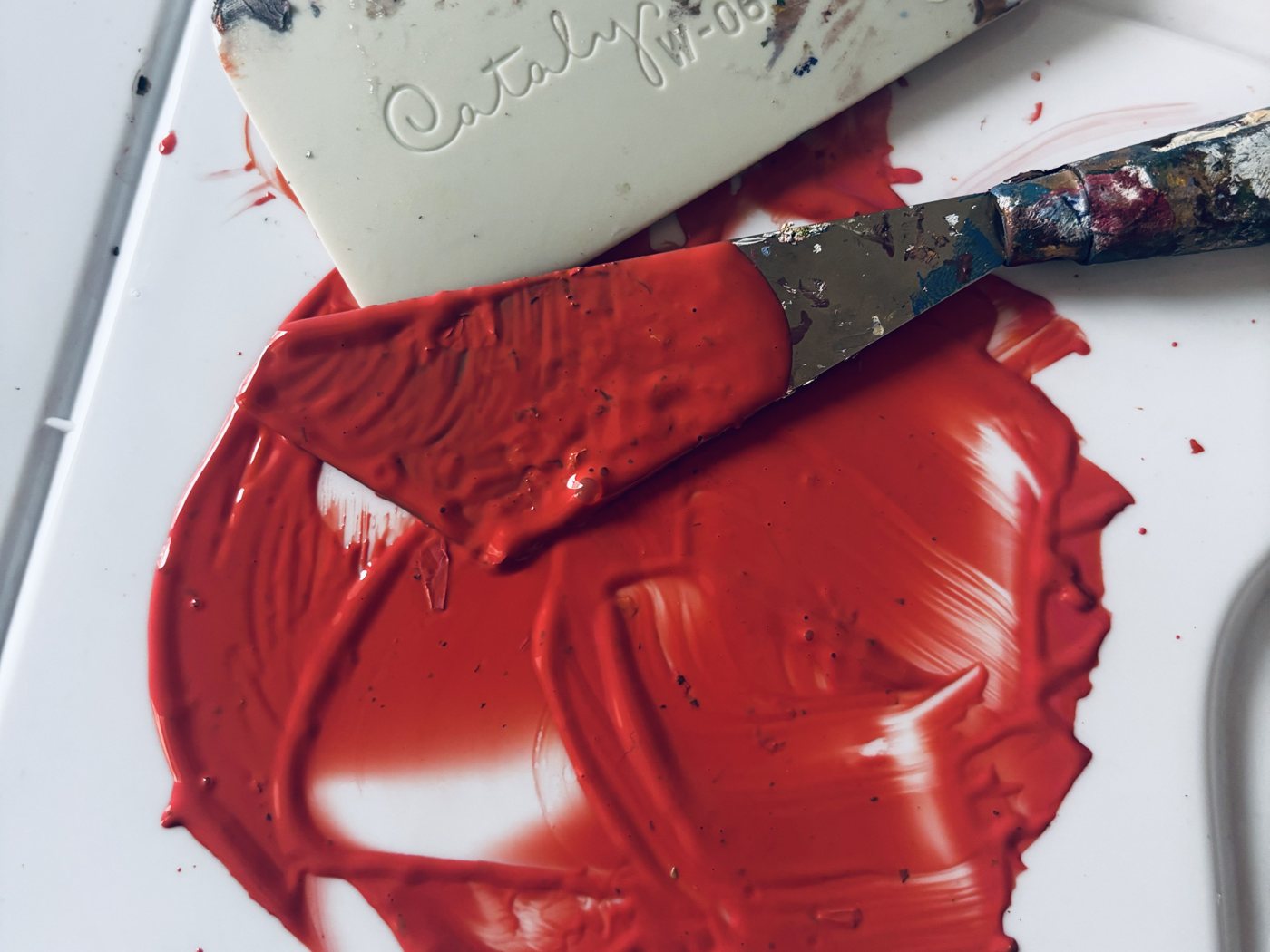 A palette knife spreading red paint on the palette