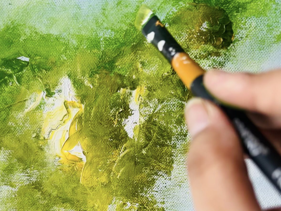 A hand working a brush of green and yellow across the canvas
